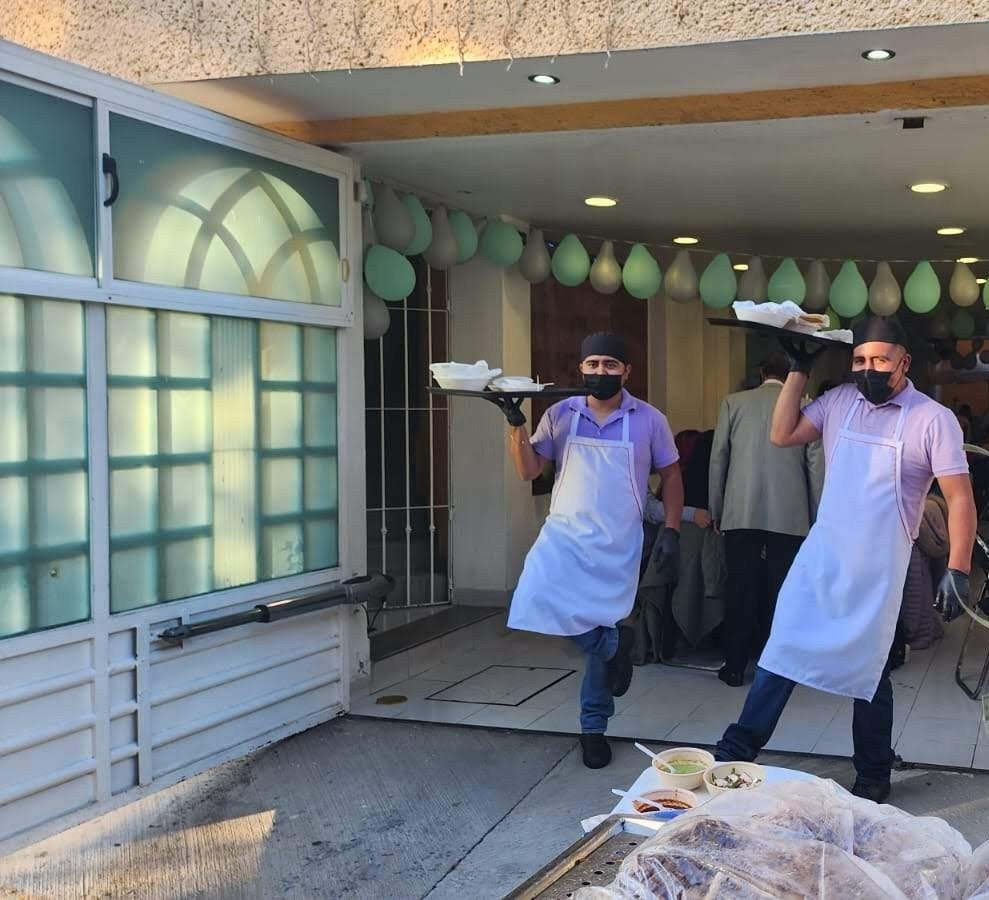 Dos meseros llevando bandejas con platos para los invitados de un evento