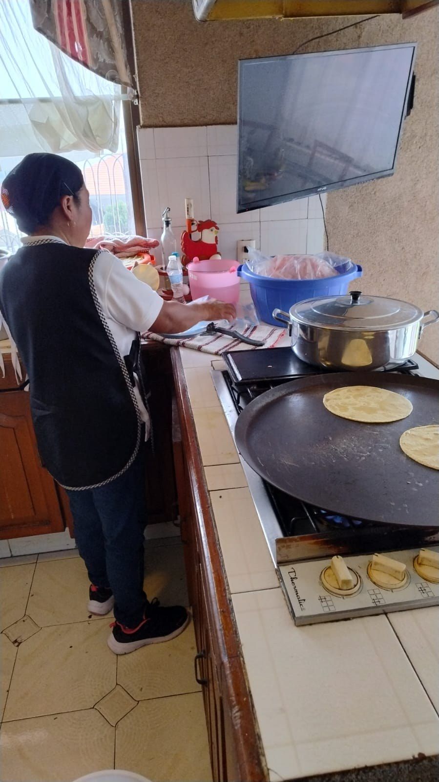 Cocinera preparando tortillas a mano junto al comal en la cocina de una casa durante un evento