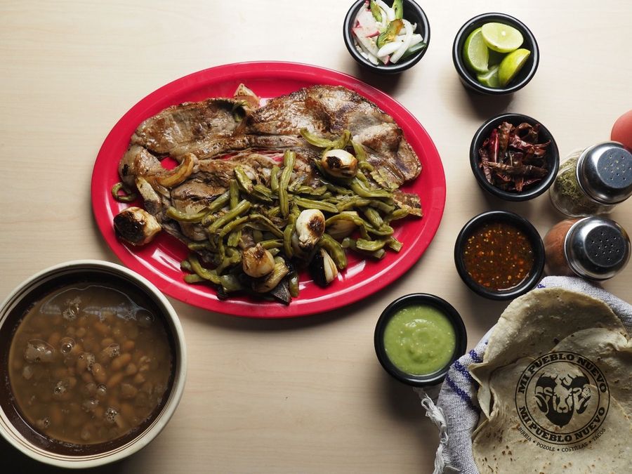 Carne asada con nopales y cebollitas cambray, con una olla de frijoles, salsas y tortillas al lado
